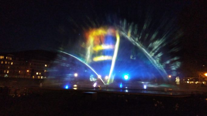Bunte Wasserfontänen mit Lichtern in einer nächtlichen Umgebung.